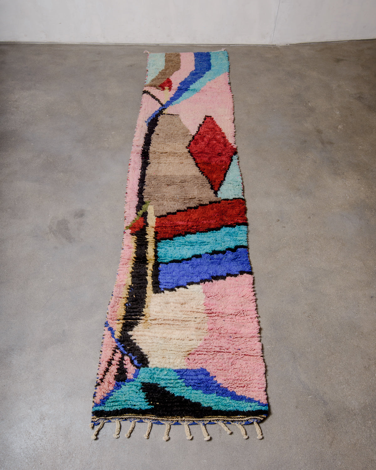 Vintage Berber runner rug made of colourful wool, laying on concrete floor.